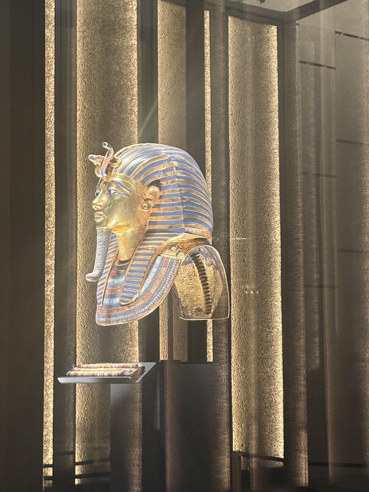 A gold pharaonic mask displayed in a glass case