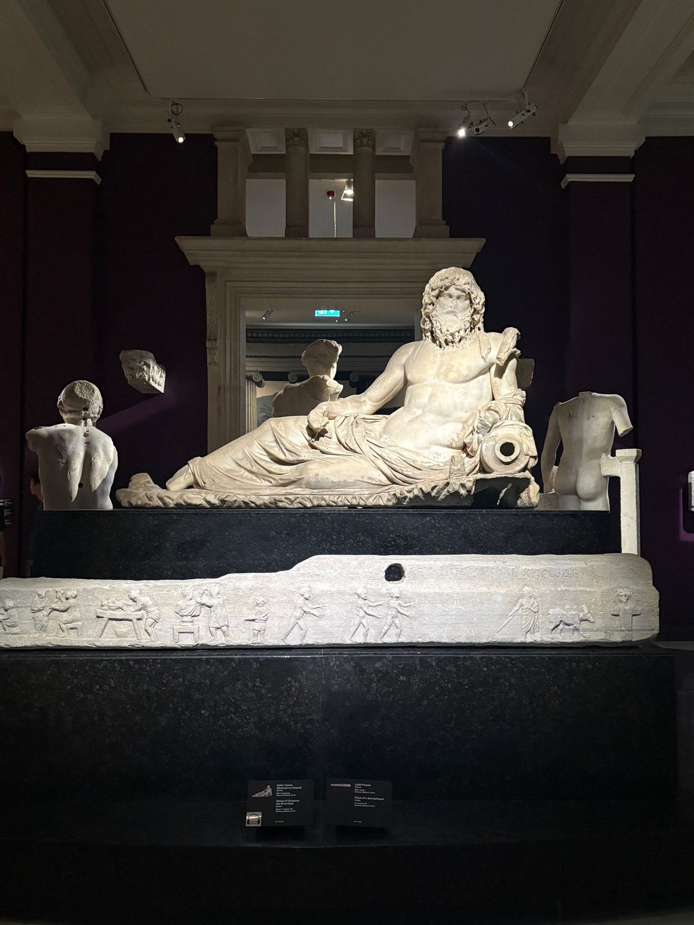 A marble reclining river-god statue in a dark museum hall