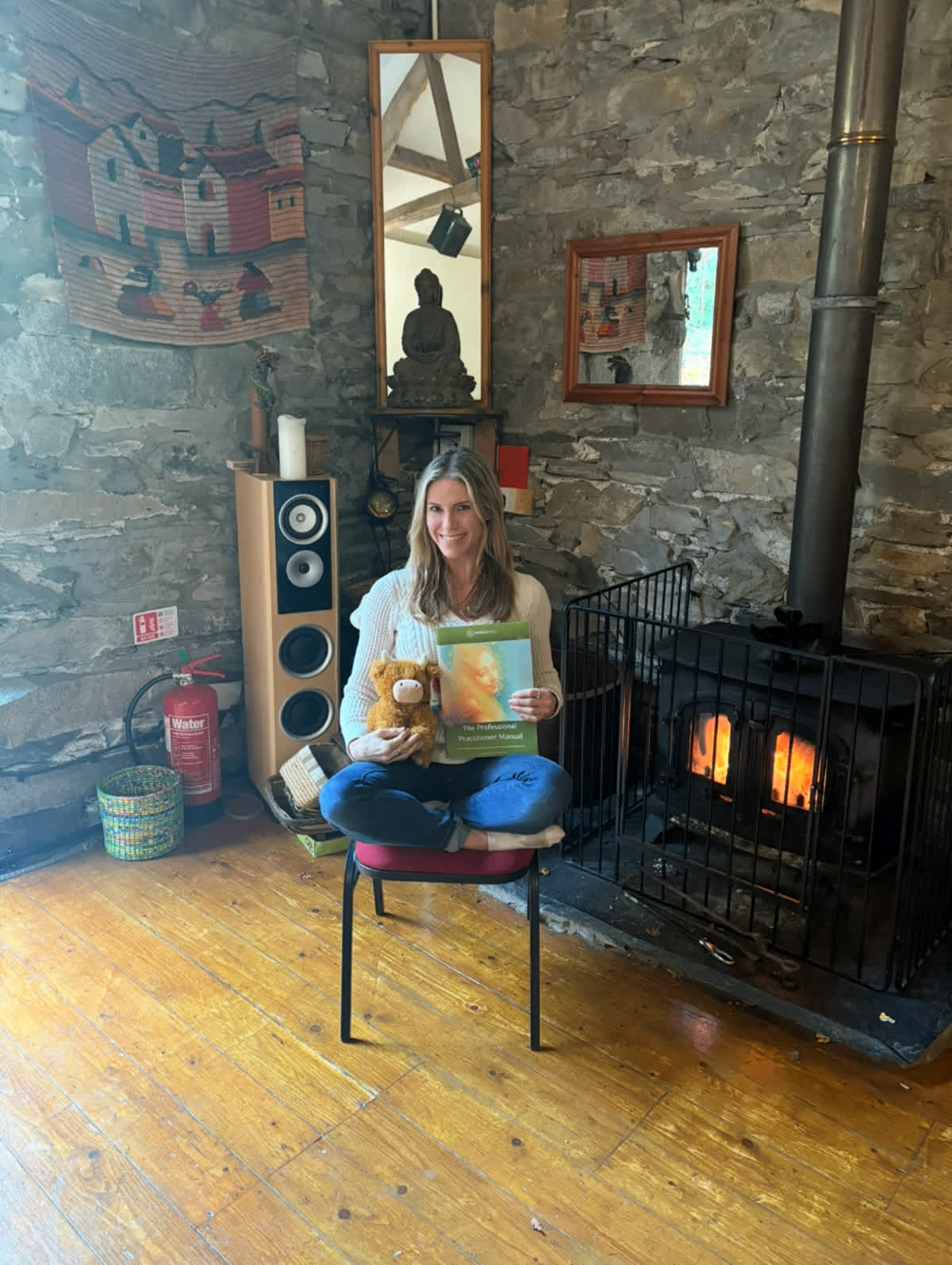 Holding the Angelic Reiki Professional Practitioner Manual and Moo Moo Mr. Cow beside a wood stove during the 10-day master workshop in the Lake District, England