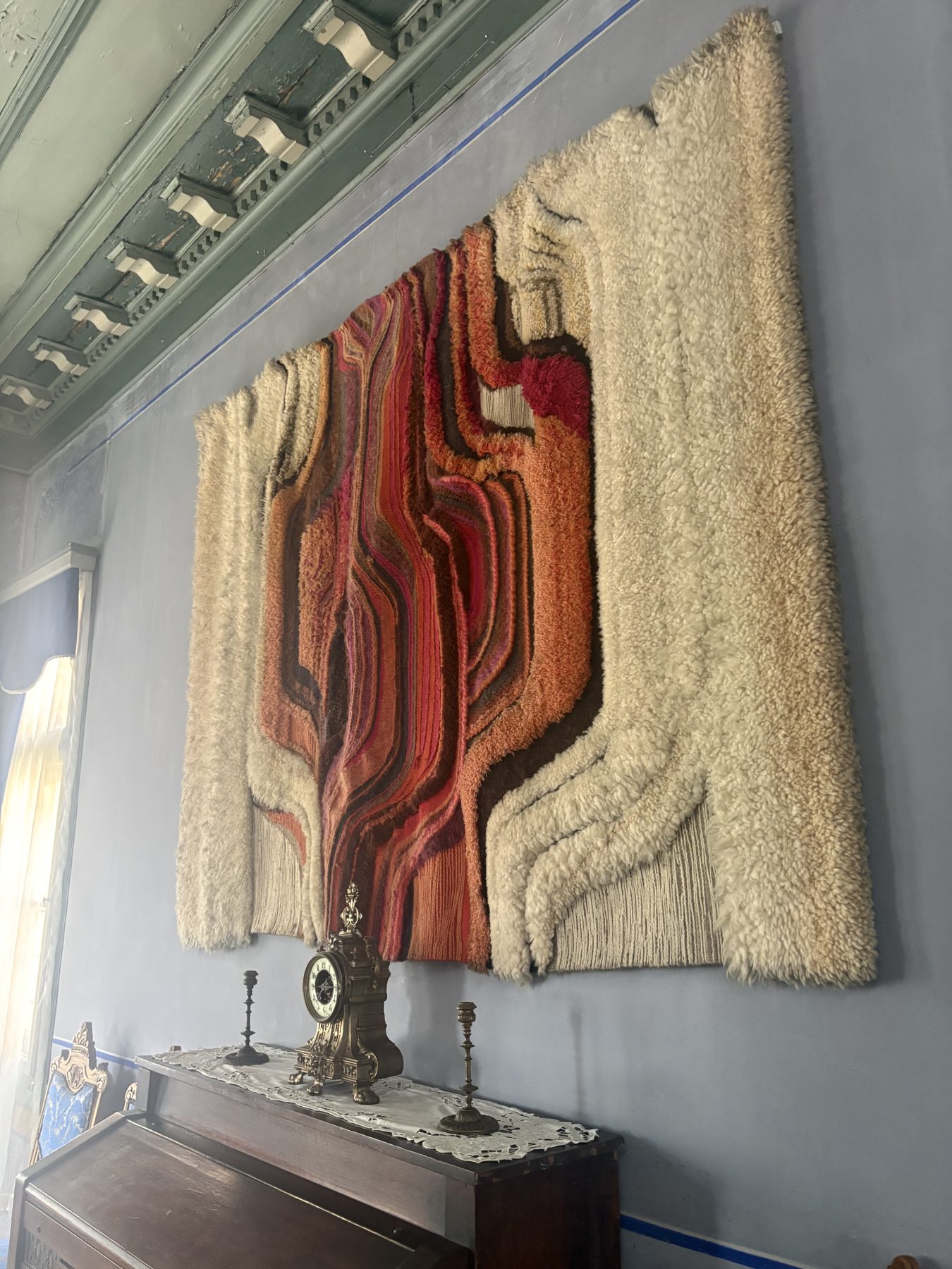 A red and cream tapestry above a table with candlesticks