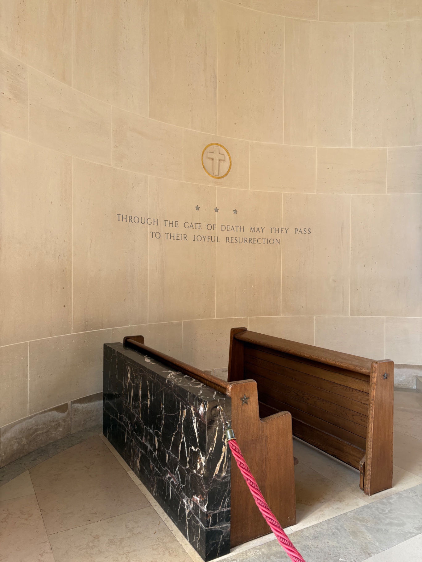 A curved limestone chapel wall inscribed 'Through the gate of death may they pass to their joyful resurrection'