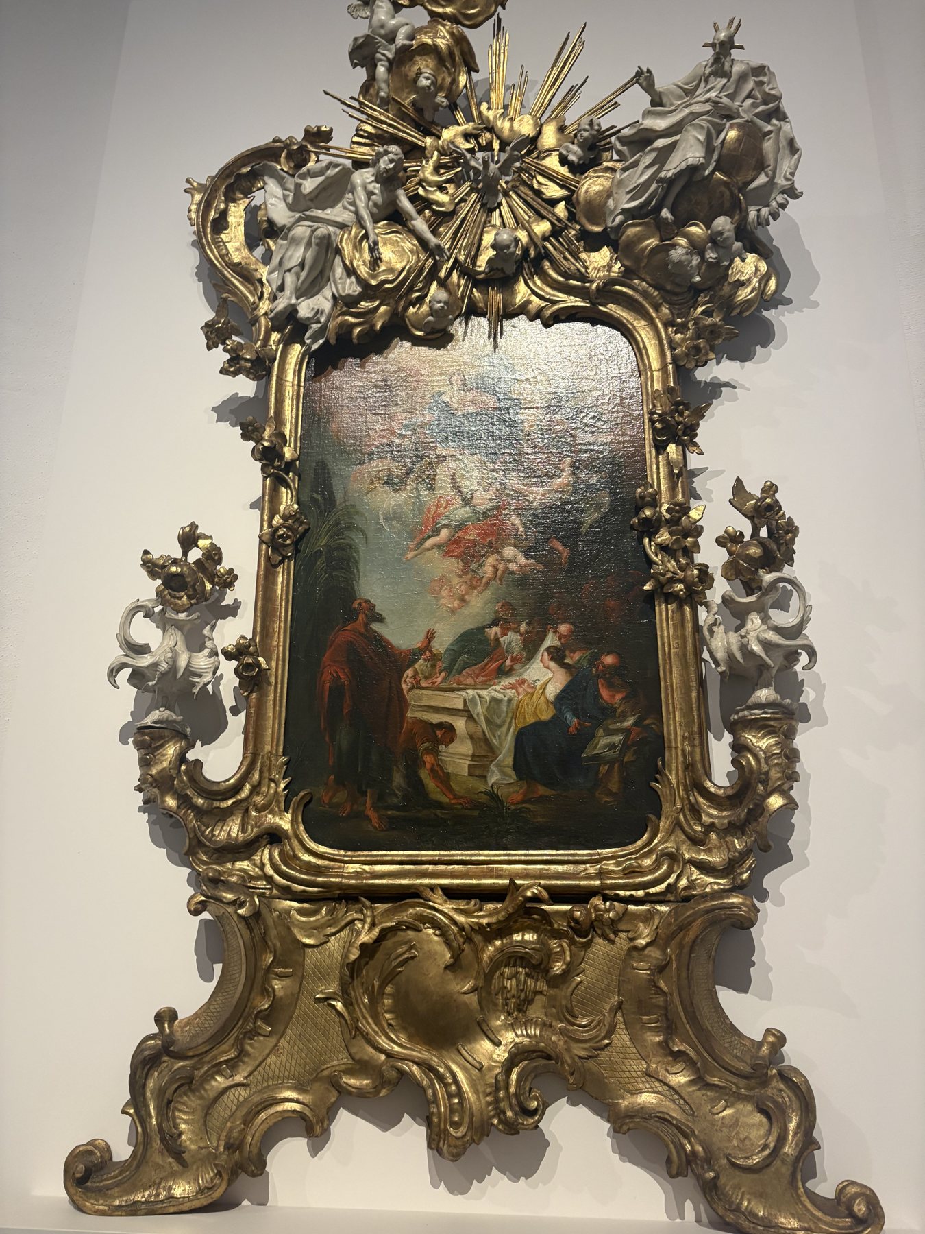 A painting in an elaborate gilded rococo frame crowned with carved rays