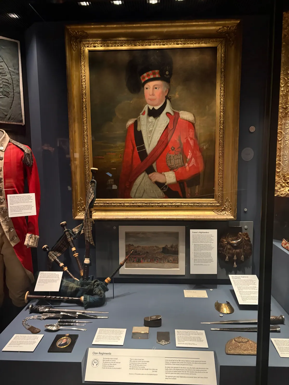 Museum case with a Highland regiment portrait, red coat, bagpipes and dirks