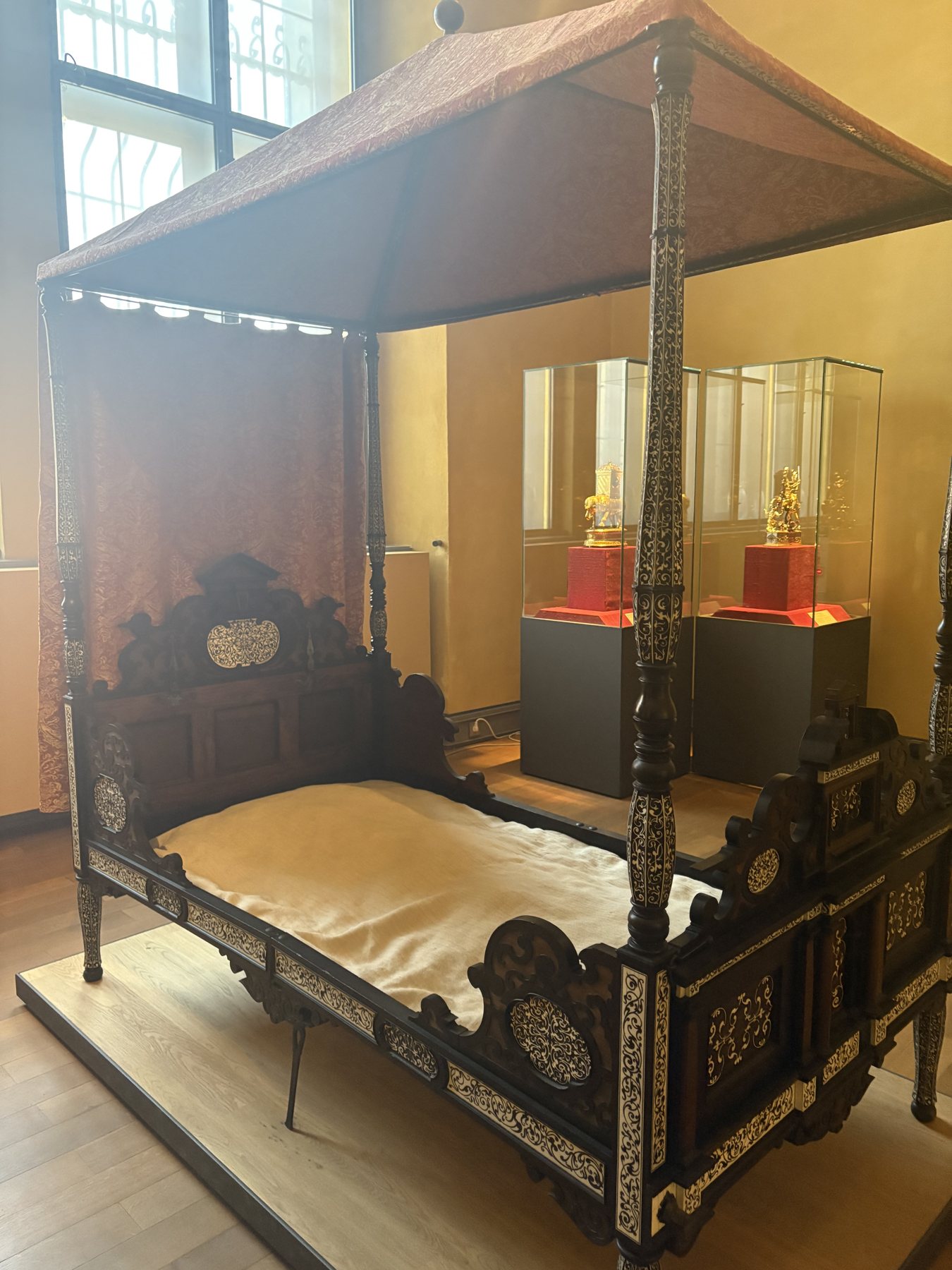A dark carved four-poster canopy bed in a museum room