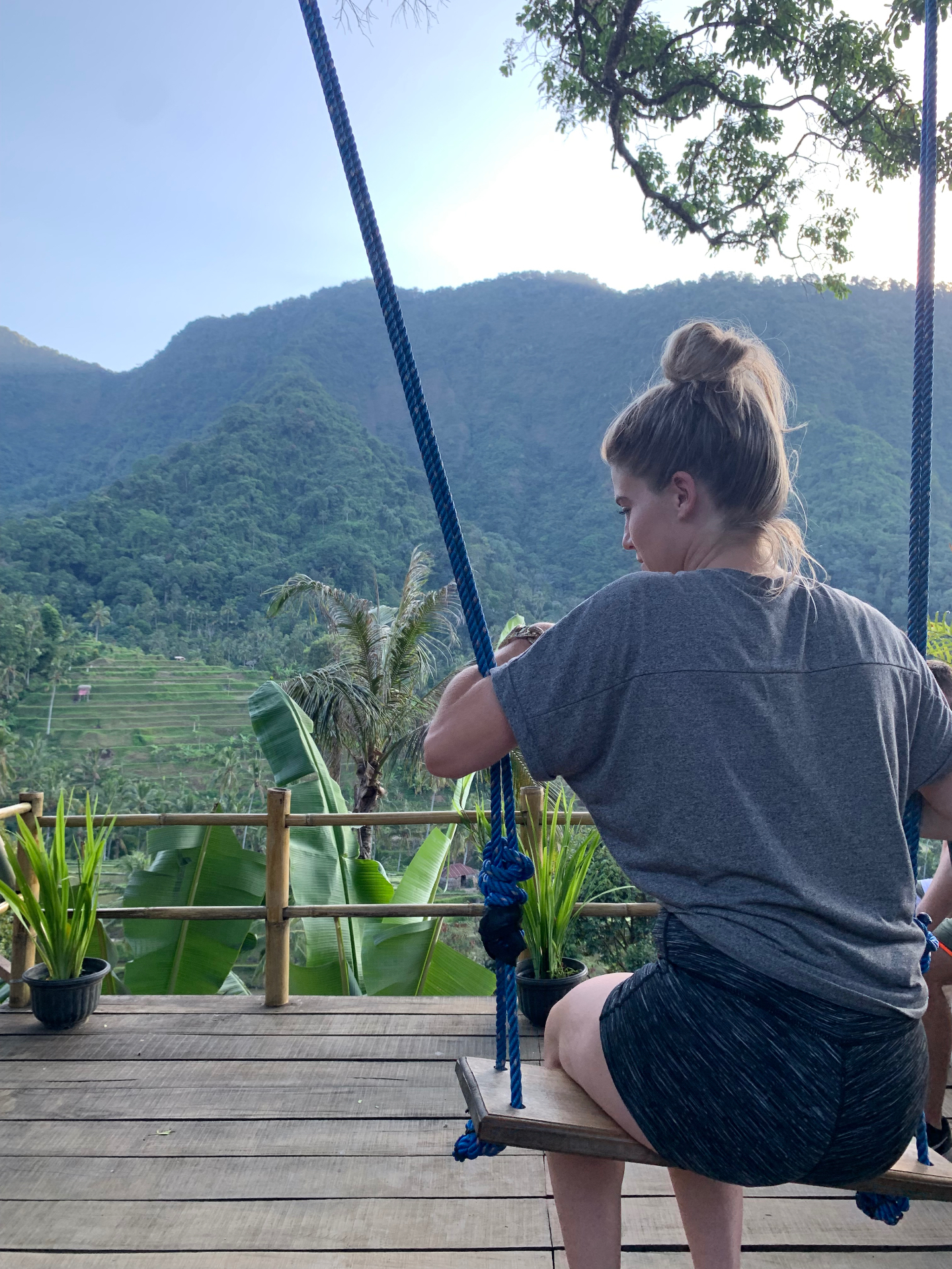 On a rope swing over Balinese rice terraces with jungle mountains beyond