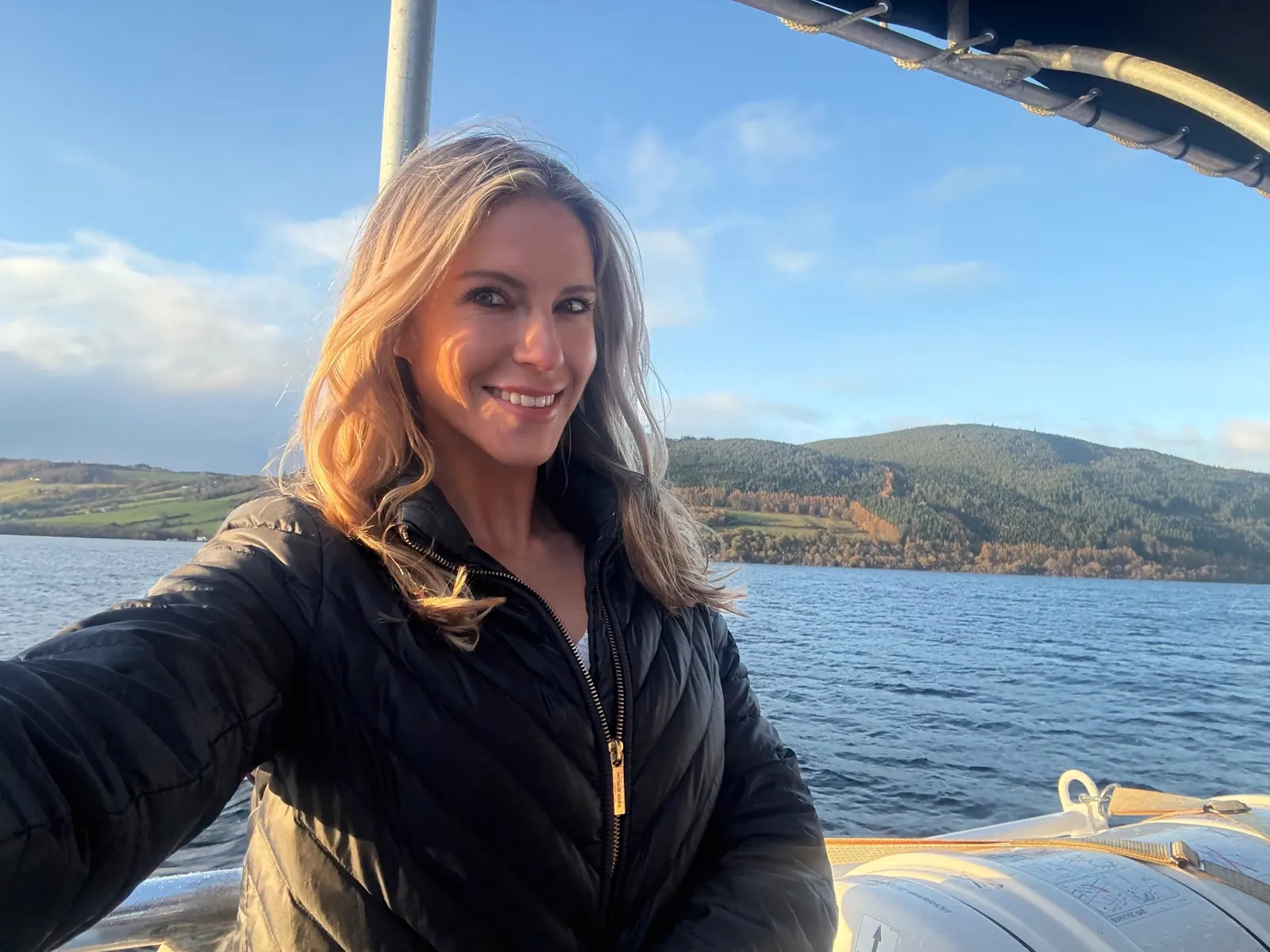 Smiling on the deck of a boat on Loch Ness with autumn hills behind