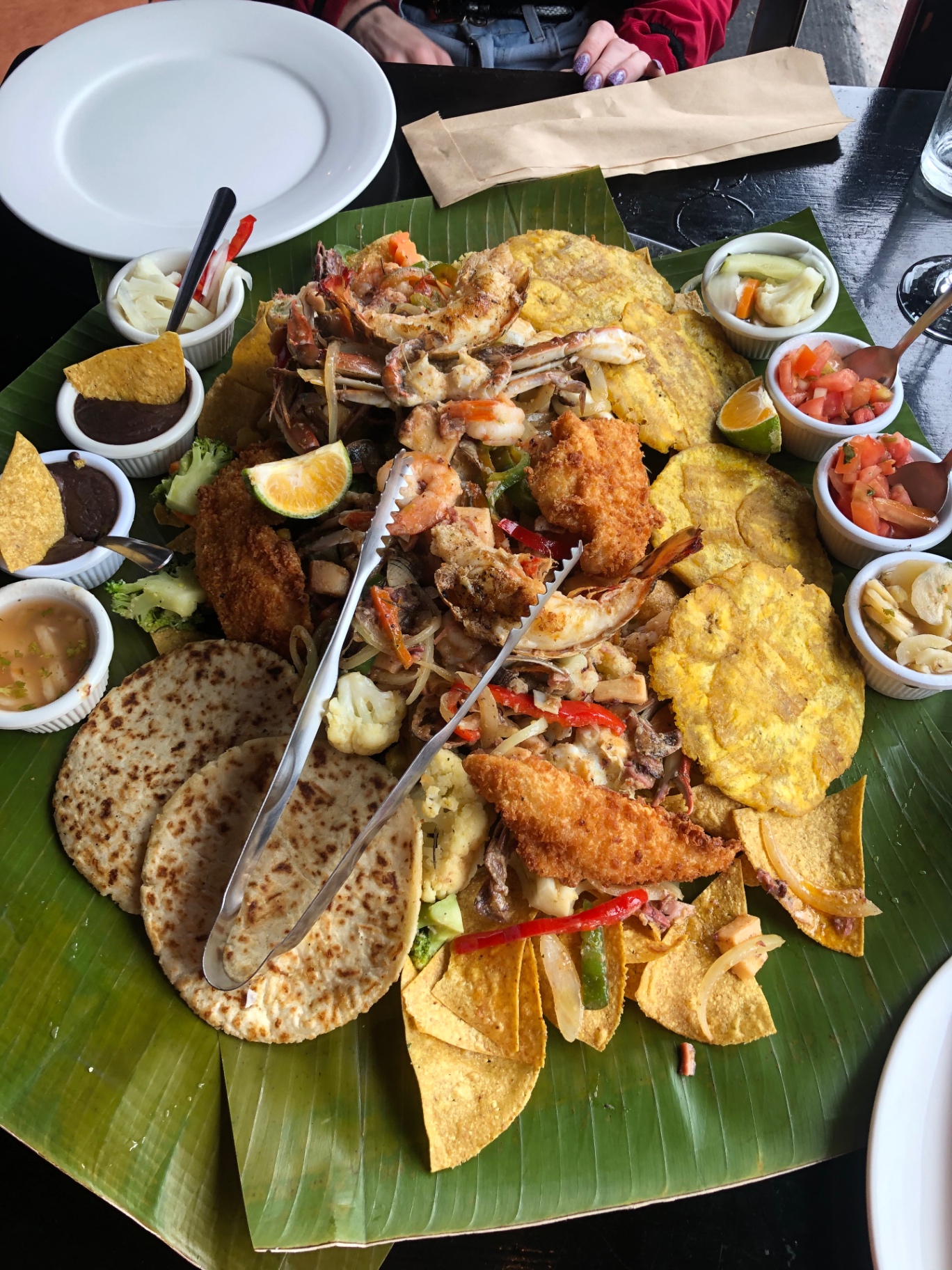 A shared seafood platter with patacones and salsas served on a banana leaf
