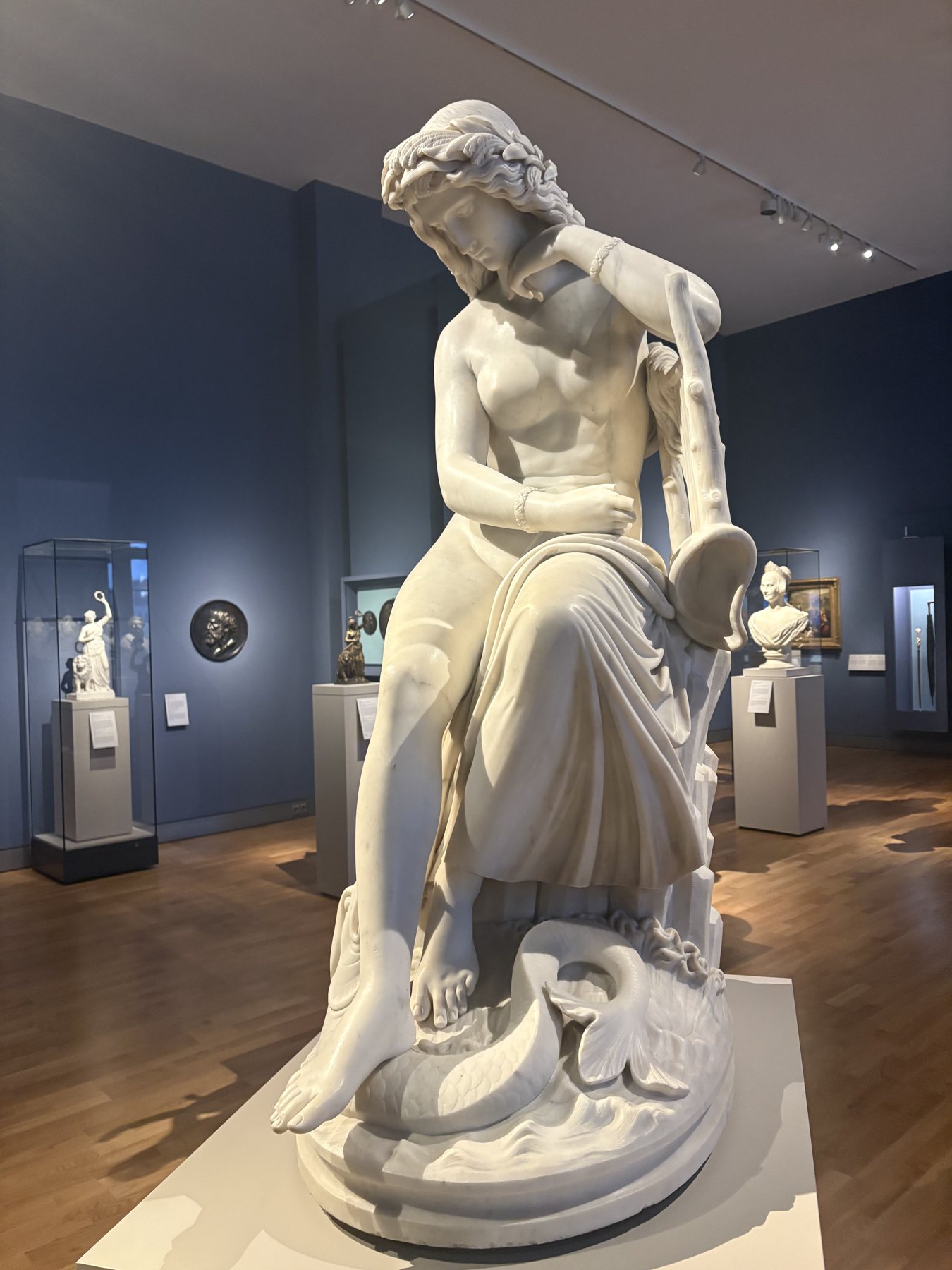 A white marble sculpture of a seated woman in a blue museum gallery
