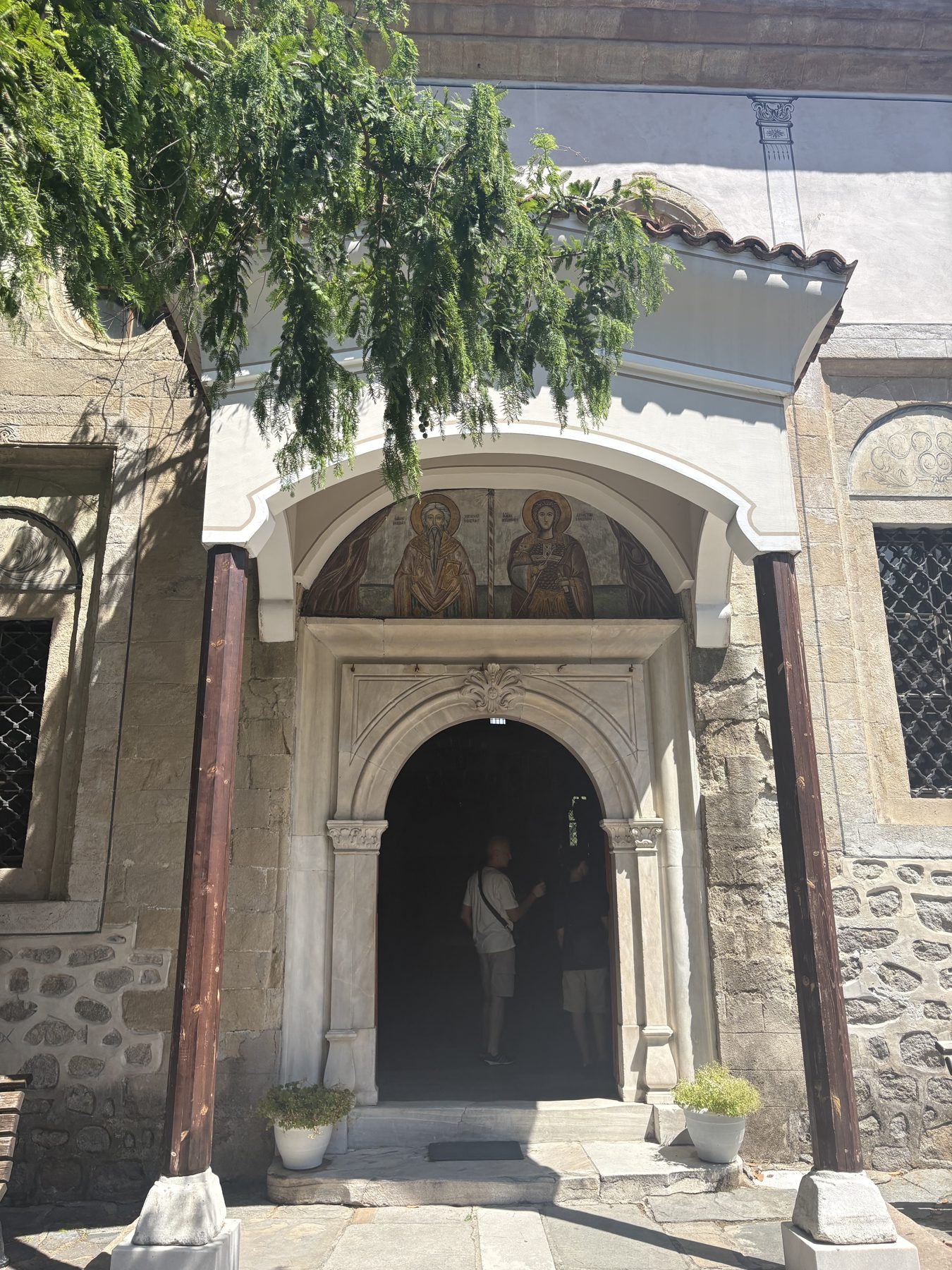 A frescoed stone church portal shaded by a tree