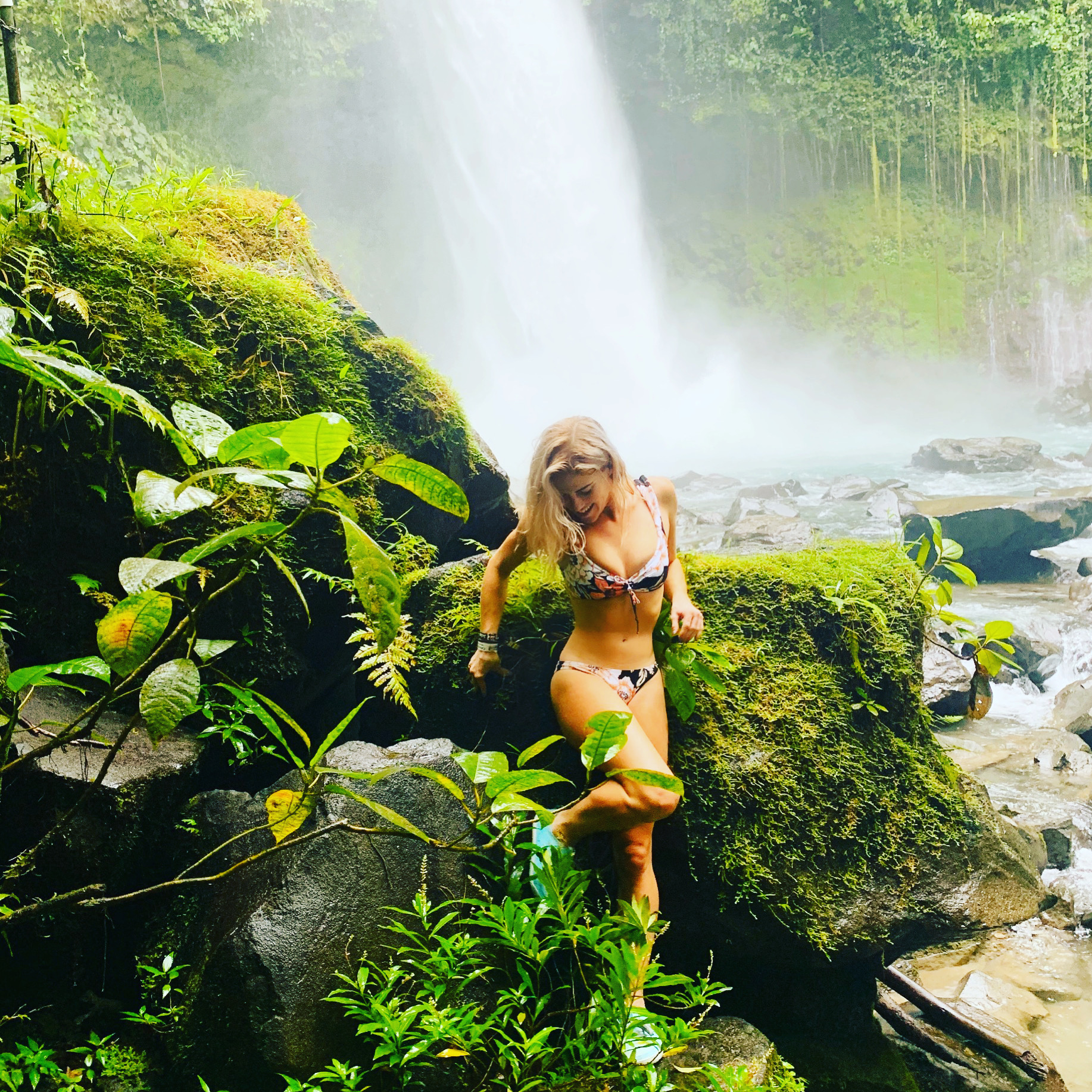Standing on mossy rocks at the base of La Fortuna waterfall