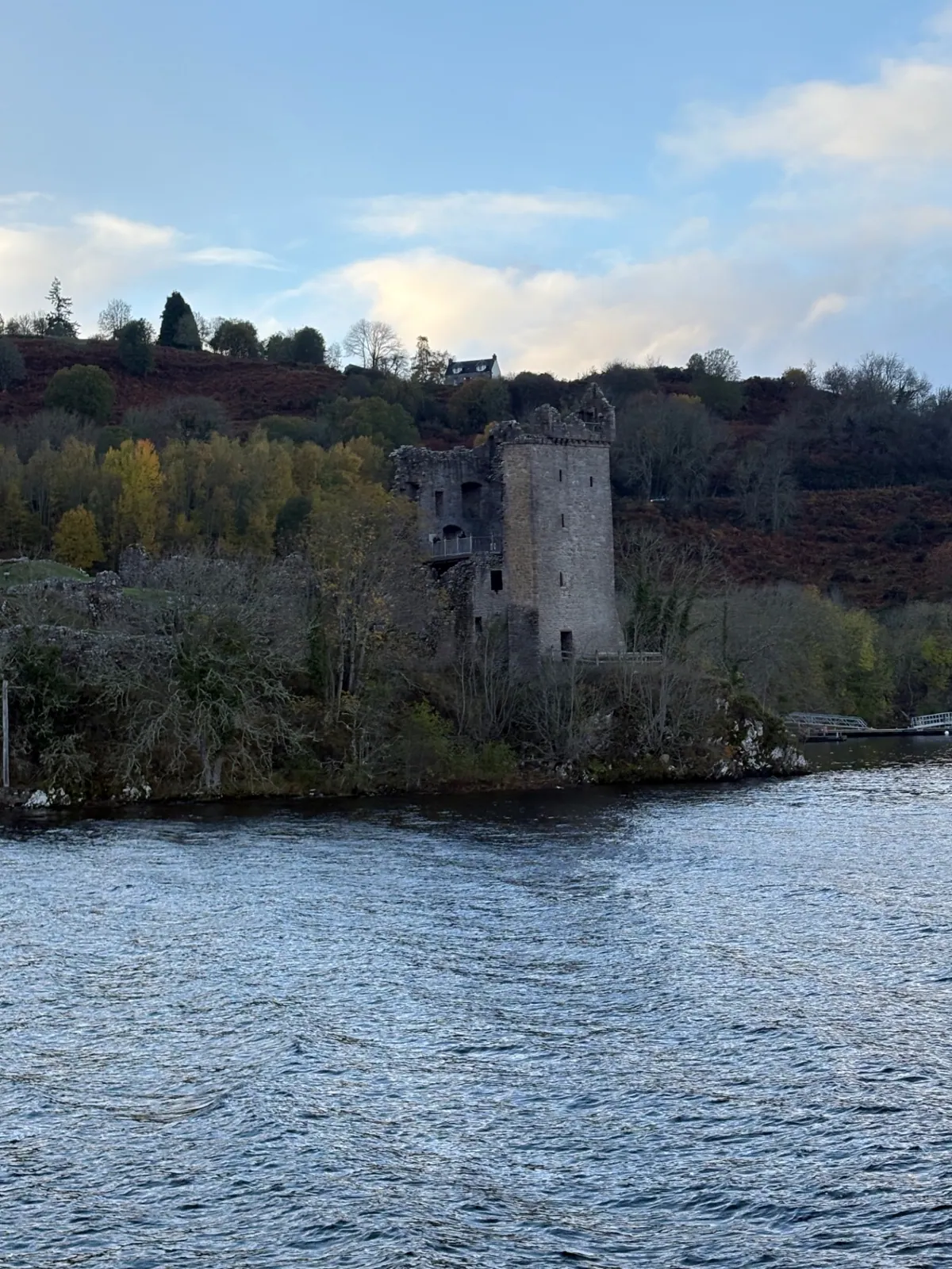 Urquhart Castle's tower seen from the water, backed by autumn woodland