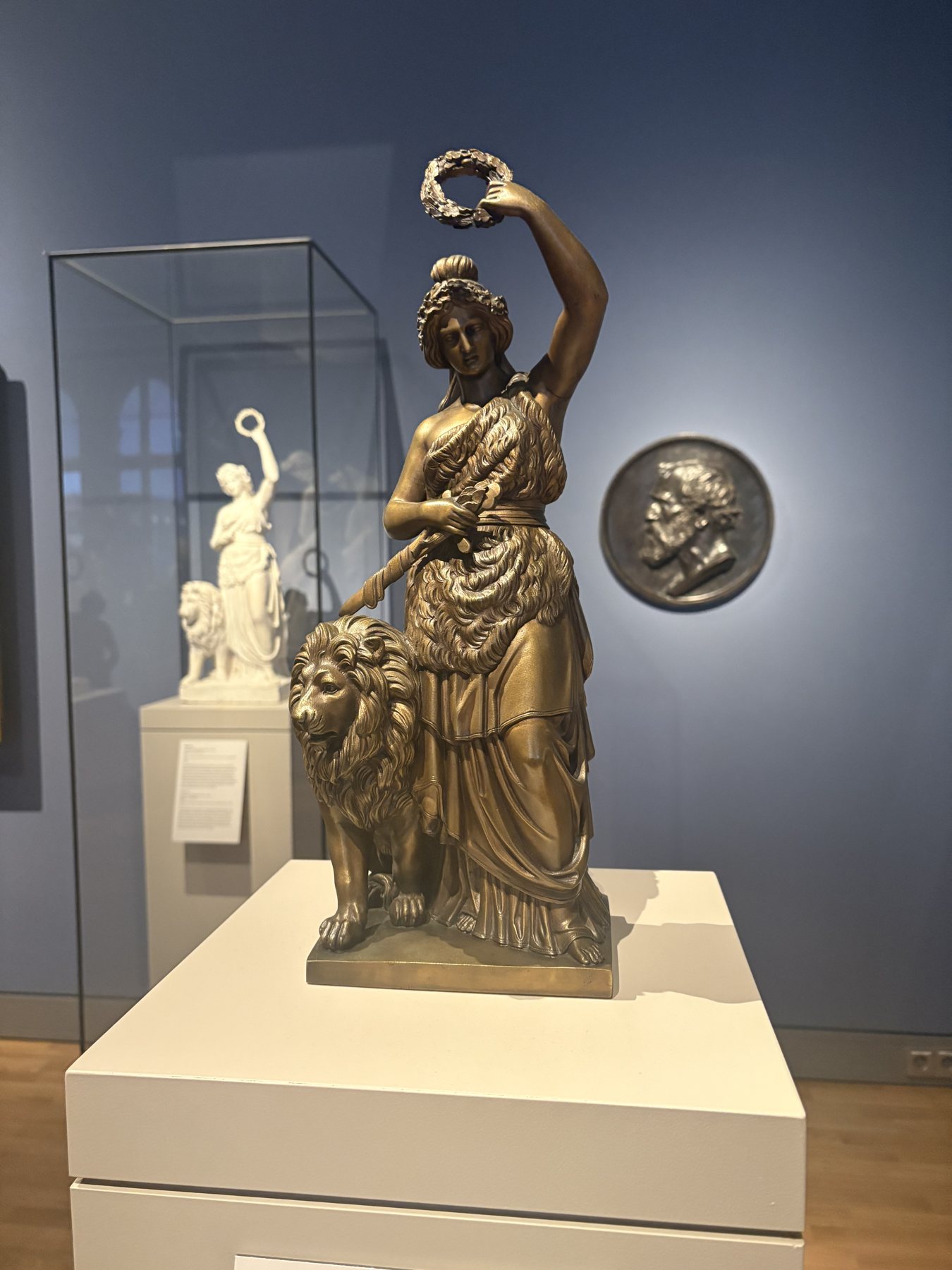 A gilded bronze female figure holding a raised object in a display case
