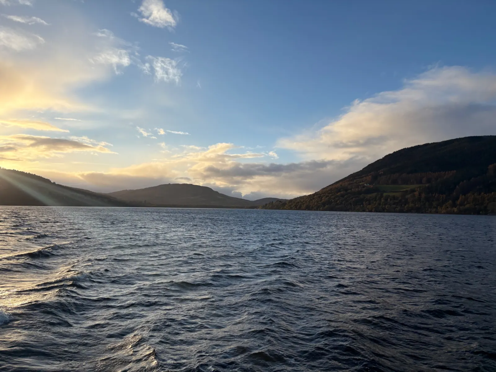 Low sun breaking over the hills at the far end of Loch Ness, wake trailing behind the boat