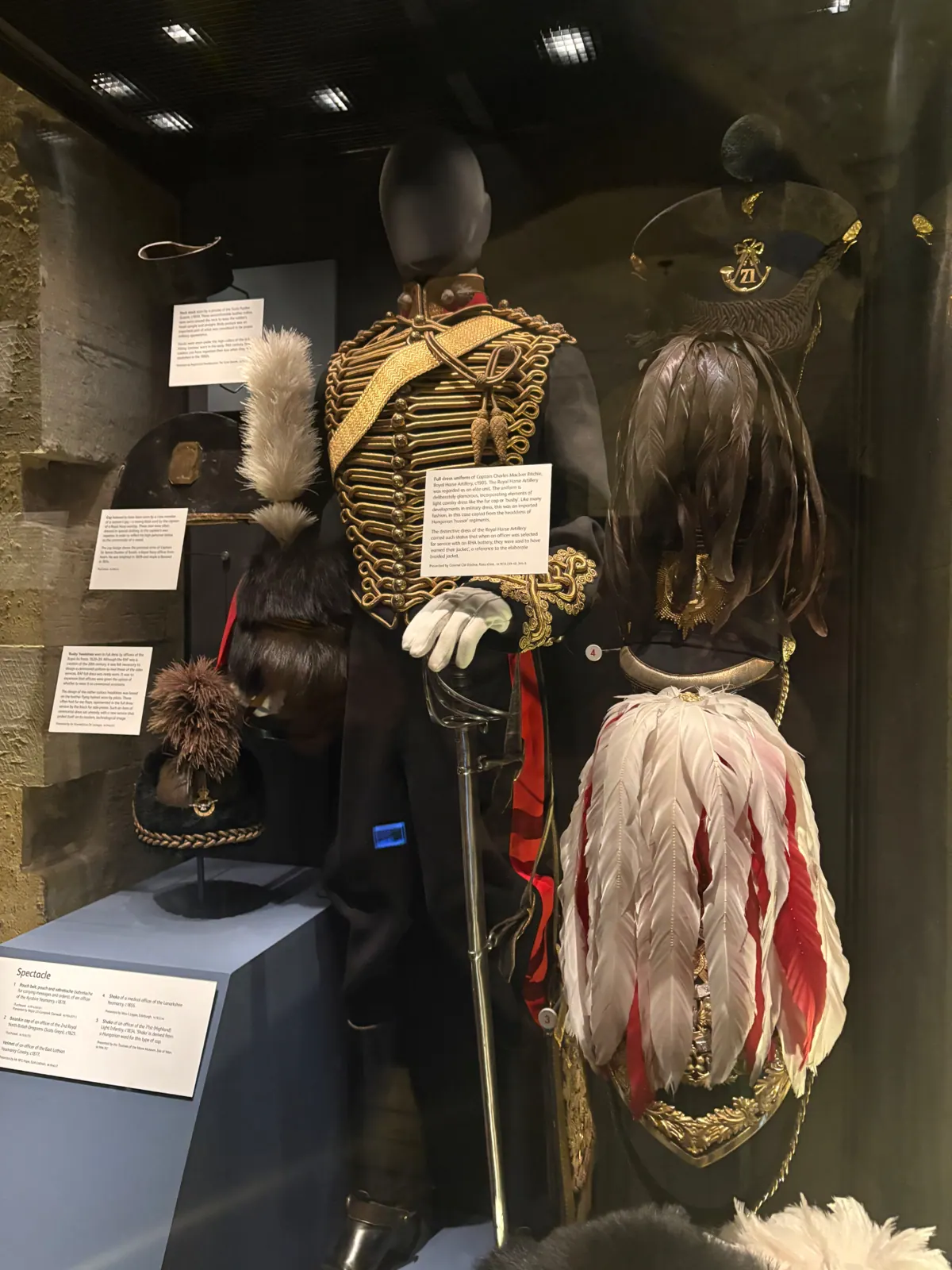 A gold-braided Royal Horse Artillery full dress uniform and plumed helmets in a museum case