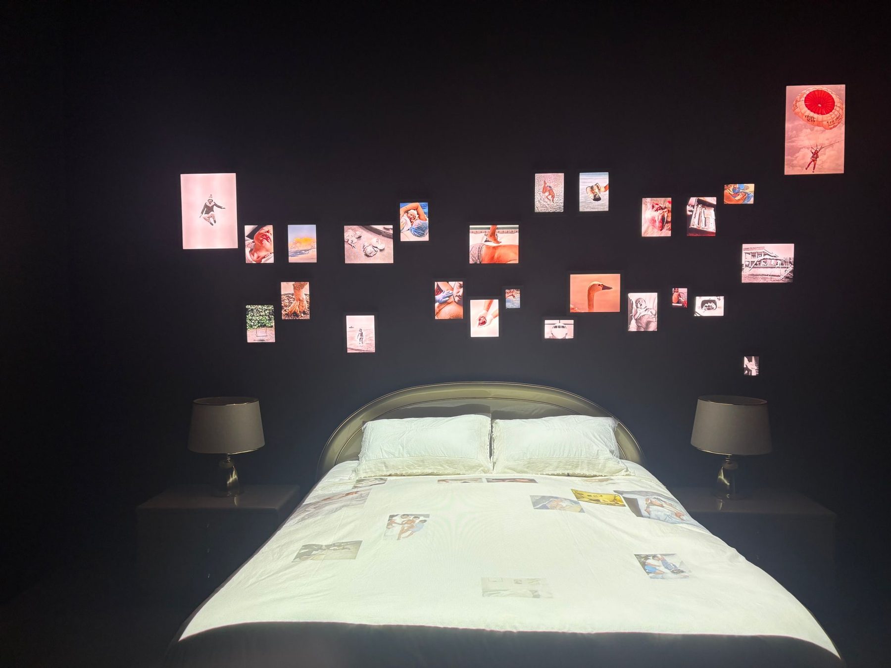An art installation of a bed beneath a wall of small photographs