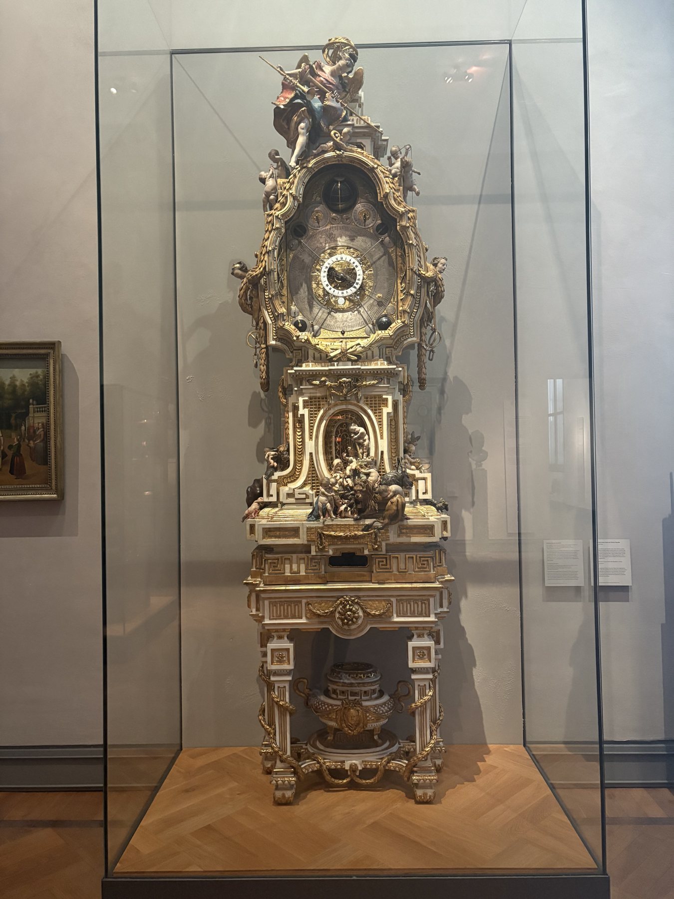 A tall gilded rococo longcase clock displayed in a glass case