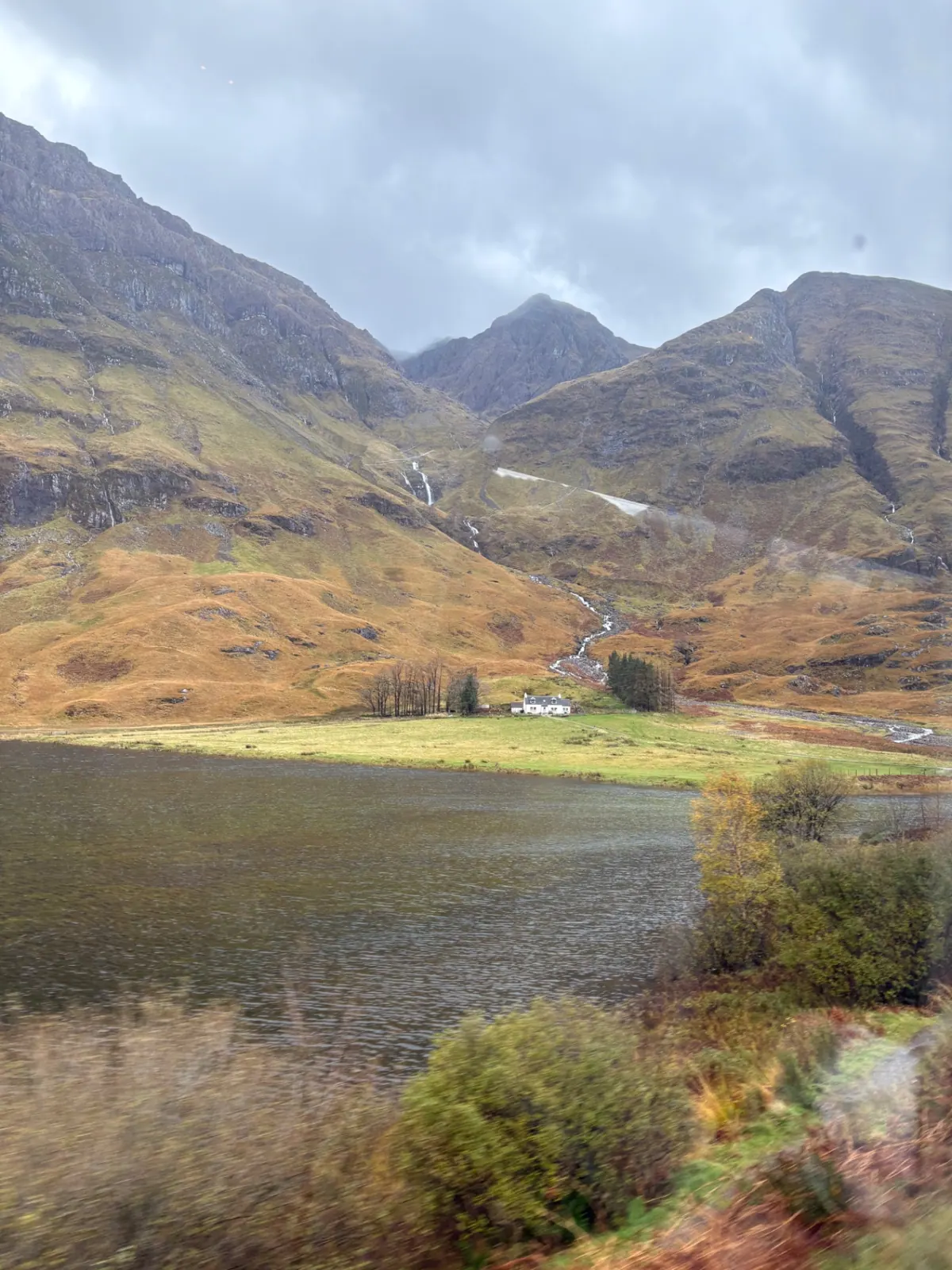 A single white cottage beneath the peaks of Glencoe with waterfalls running down the slopes