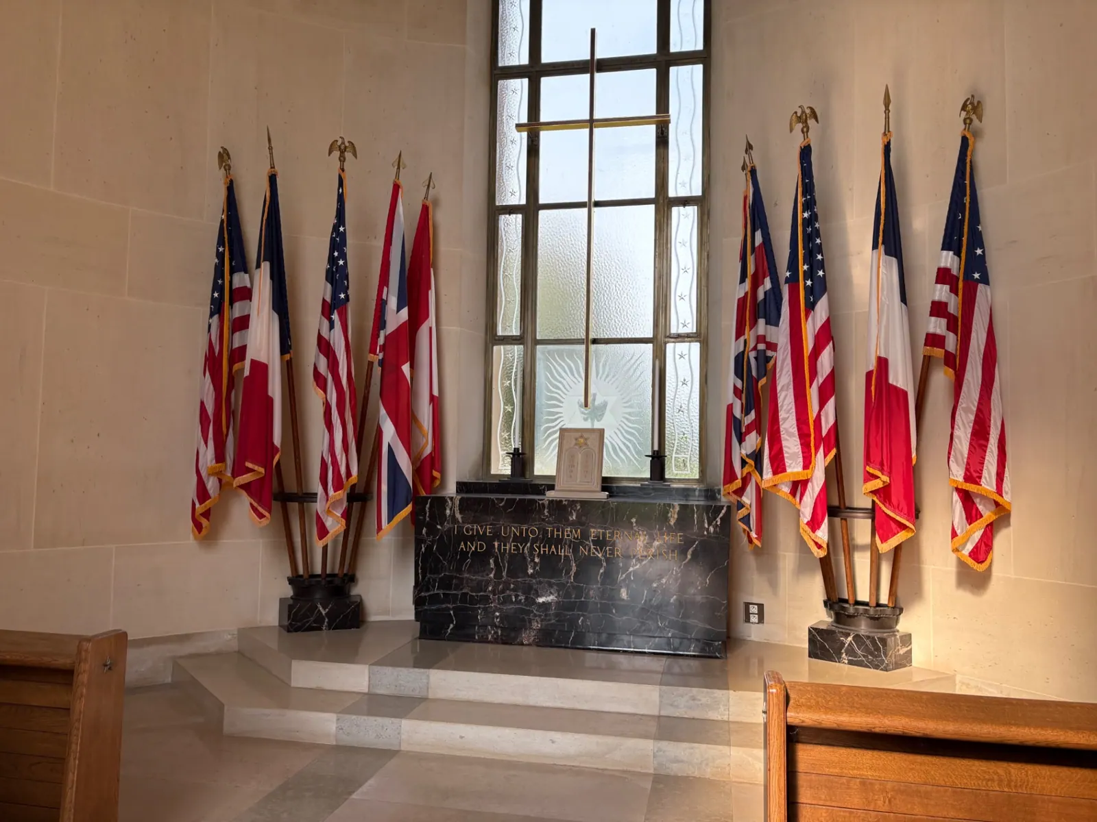 The memorial chapel altar flanked by American, French and British flags beneath a tall window with a dove