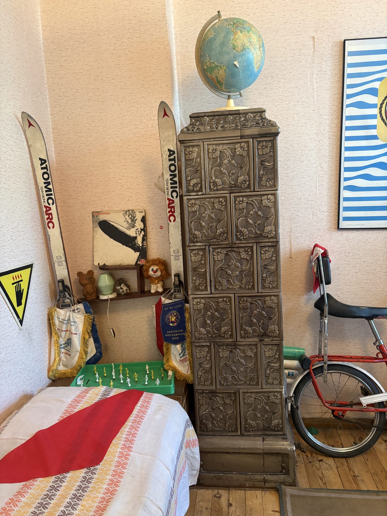 A socialist-era apartment corner with skis, a globe and a tiled stove