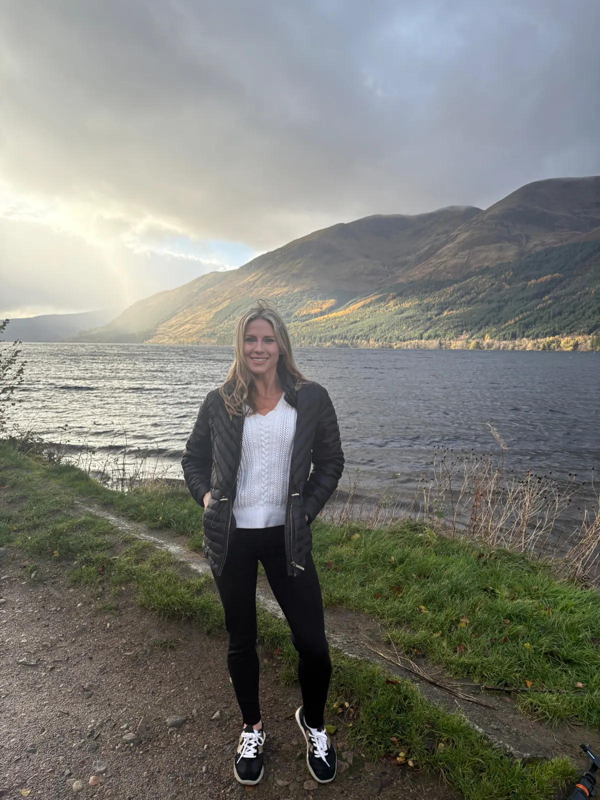 Standing at the edge of a Highland loch with a faint rainbow breaking through cloud