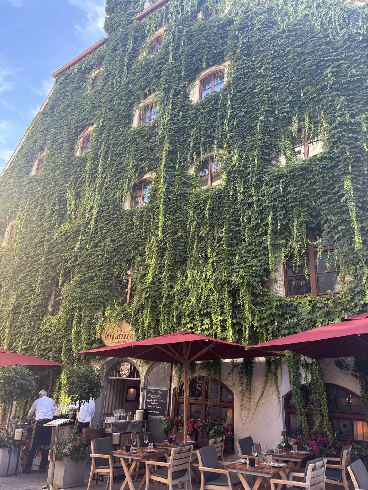 A Munich building covered in trailing ivy above a terrace of café tables