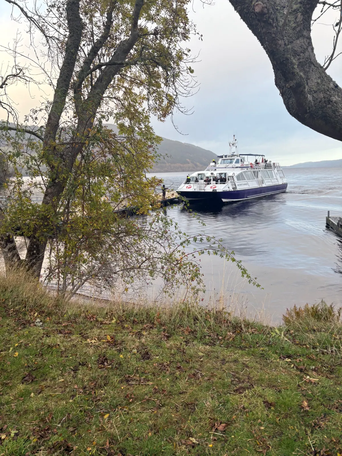 A Jacobite cruise boat pulling into a wooden jetty on a grey Loch Ness morning