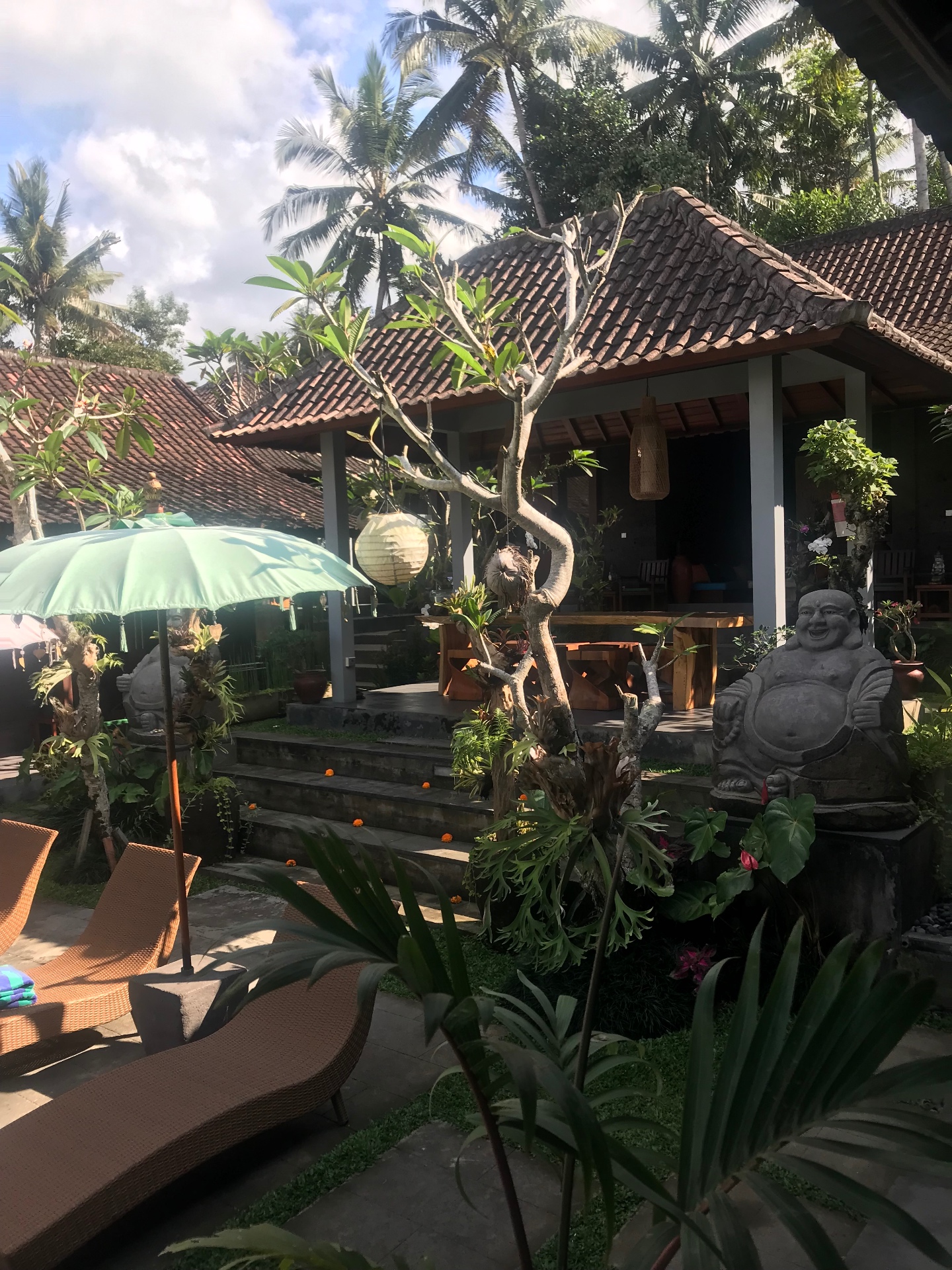 Ubud garden with stone Buddha statues, frangipani trees and tiled pavilions