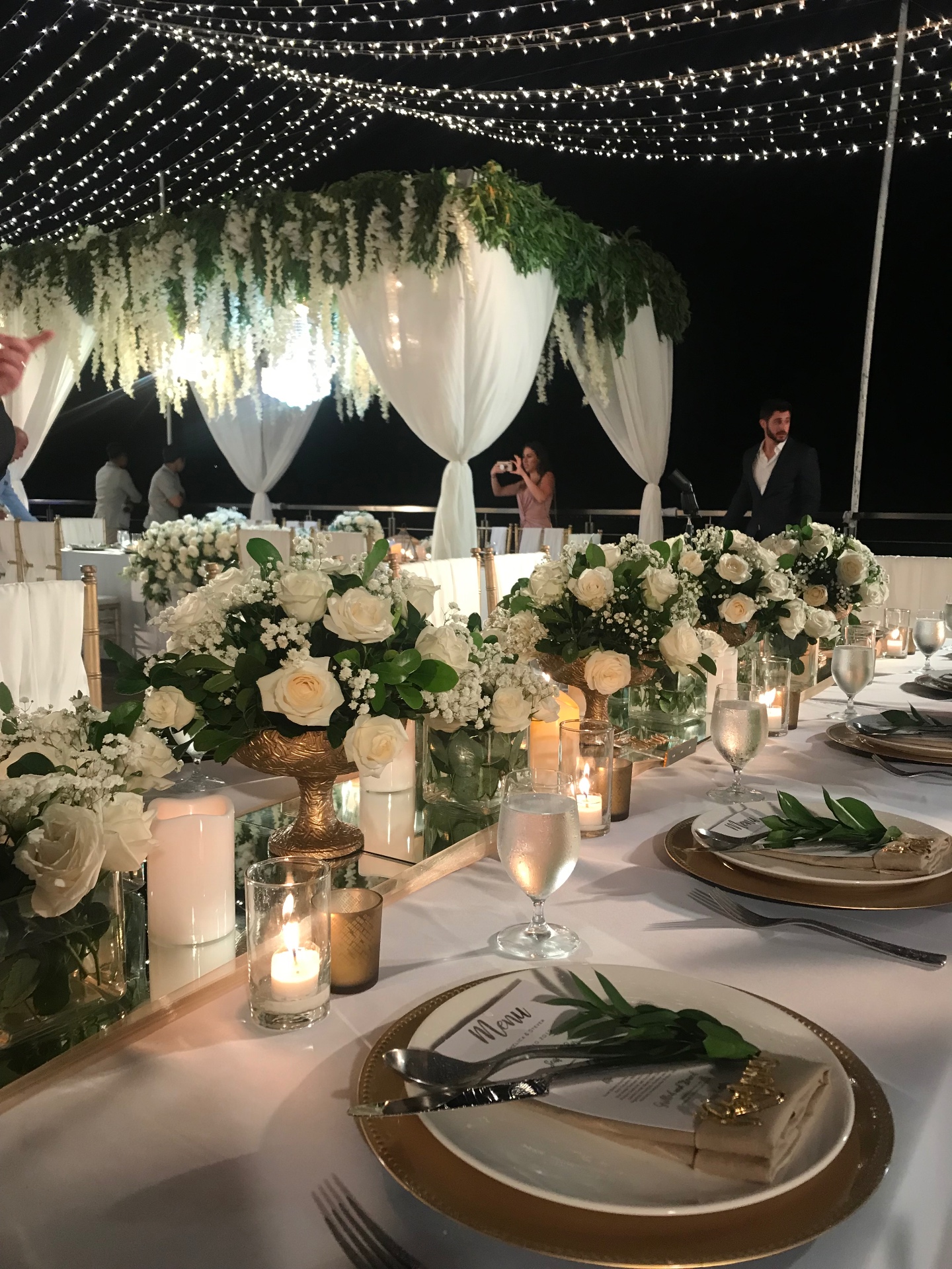 Wedding reception table with white roses, candles and fairy lights at night