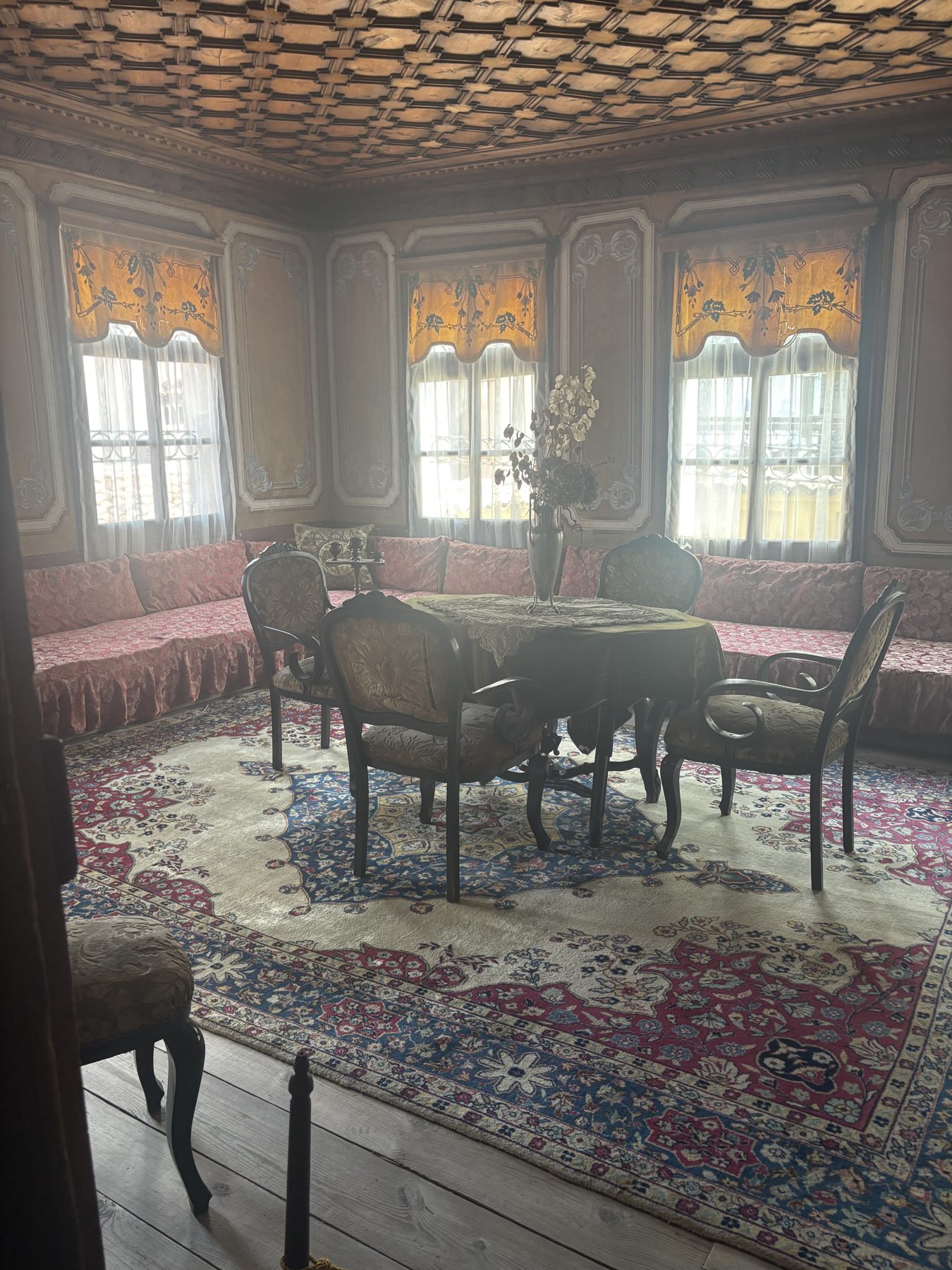 A preserved Revival-era salon with carved ceiling and patterned carpets