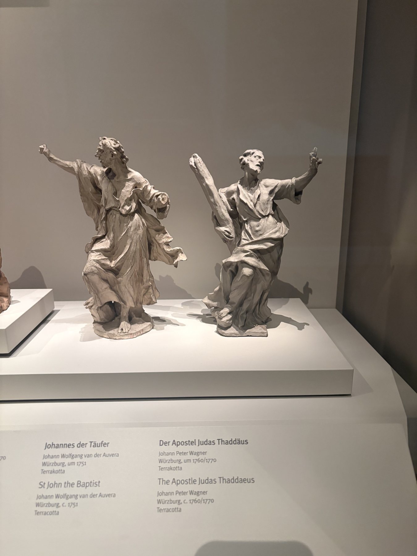 Two silver apostle figures with raised arms on a museum plinth